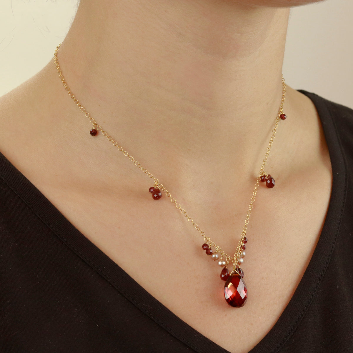 Elegant garnet, zircon, and pearl pendant worn on model, showcasing a vibrant gemstone combination in a sophisticated design.