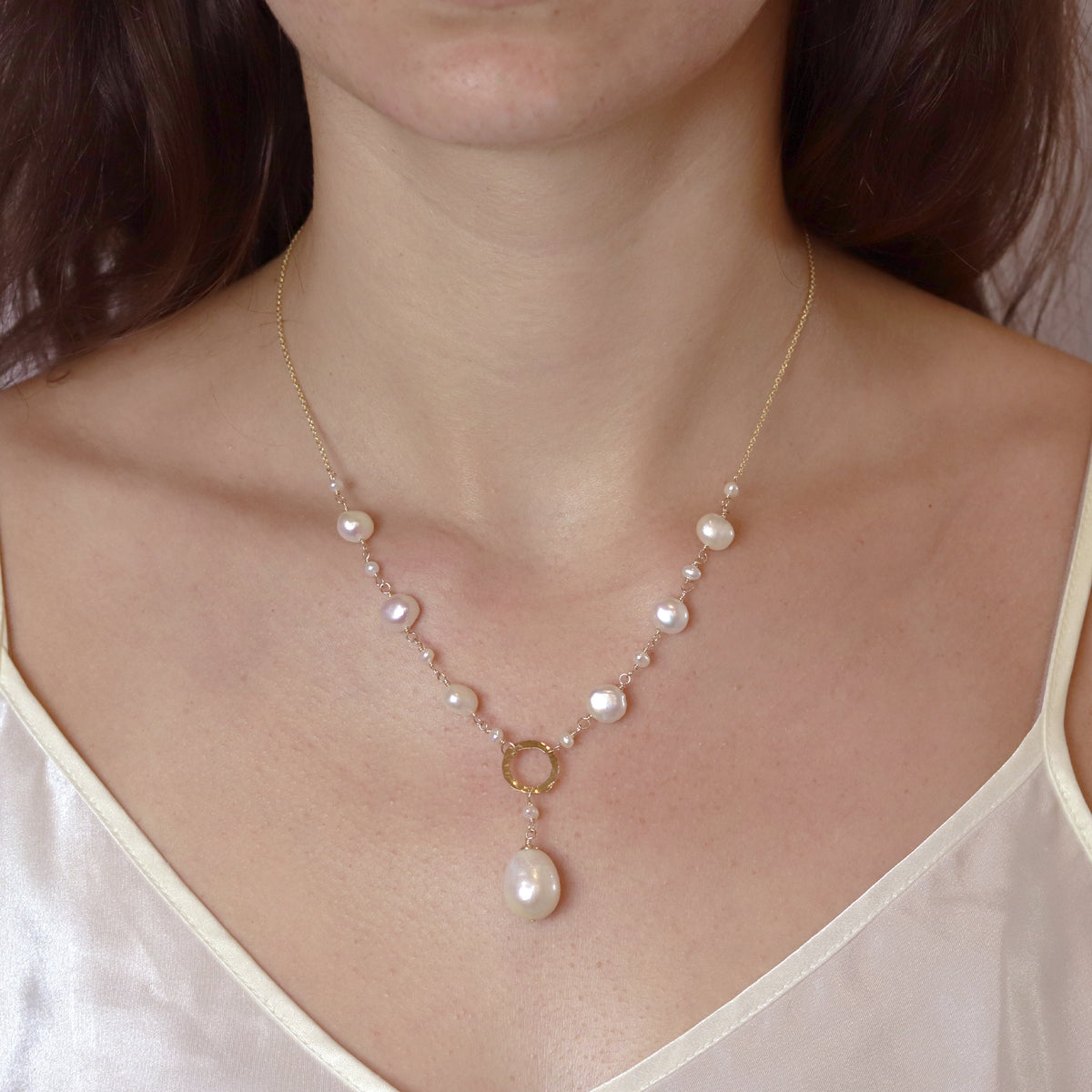 Model wearing a Y-shaped necklace with a hammered circle pendant and a pearl accent, adding a modern and elegant touch to any outfit.