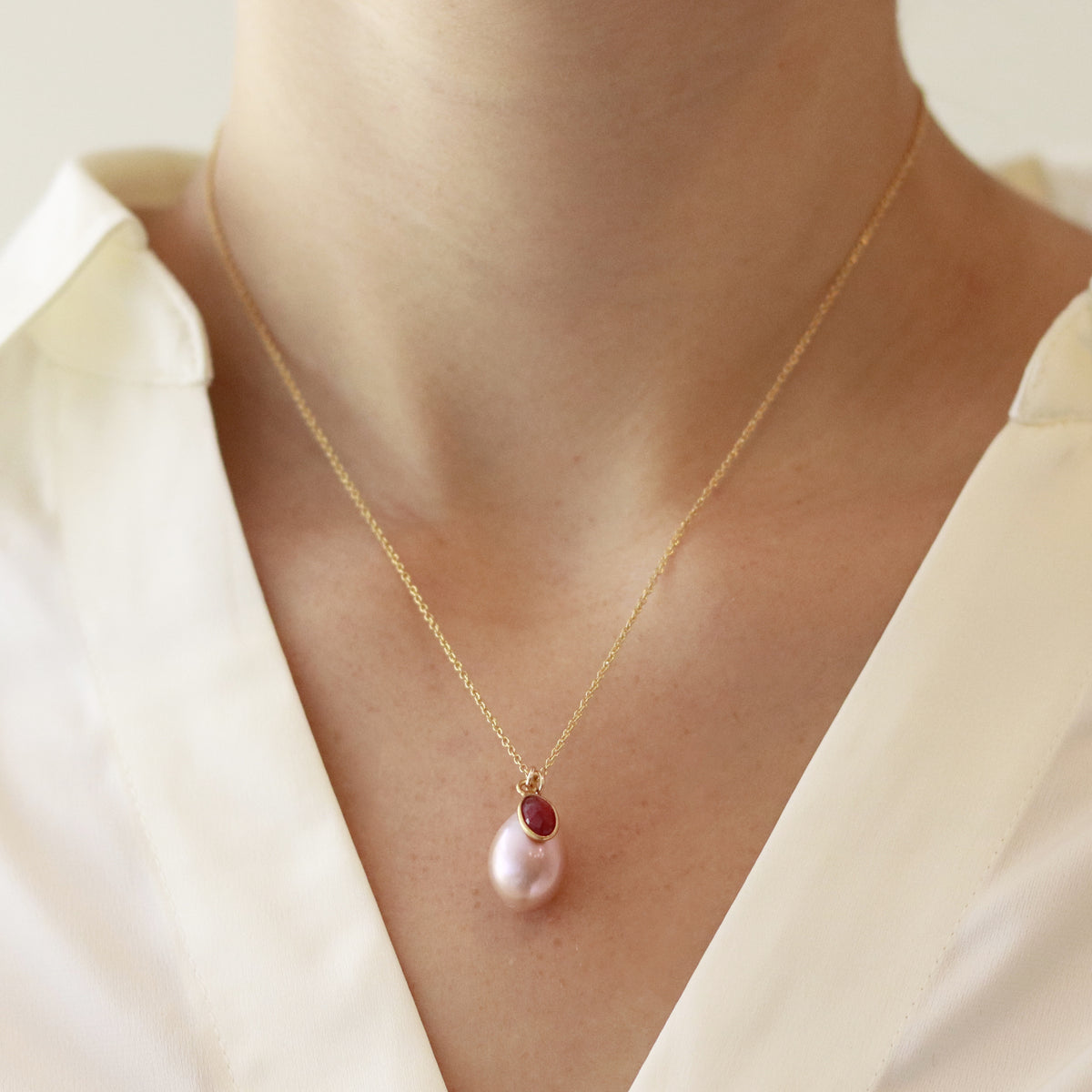 Pink pearl and ruby pendant necklace in gold, elegantly worn by a model, showcasing its timeless and delicate design.